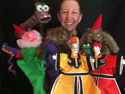 UConn Online Graduate Certificate Graduate and Student Amy West shares her story while holding many puppets while smiling.